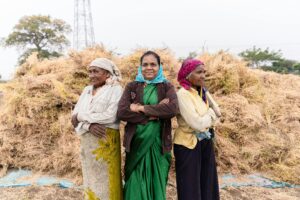 Three women farmers standing proud amidst harvested crops in rural India.